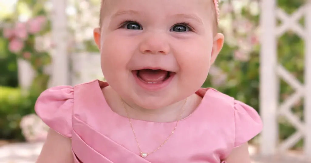 baby girl in pink dress wering her Add A pearl necklace sitting outddors