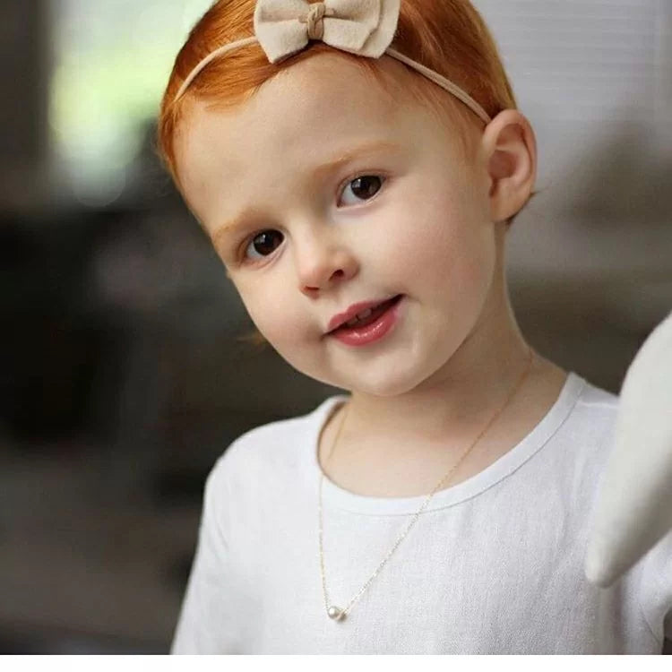 Young girl with red hair wearing a necklace with a single pearl.