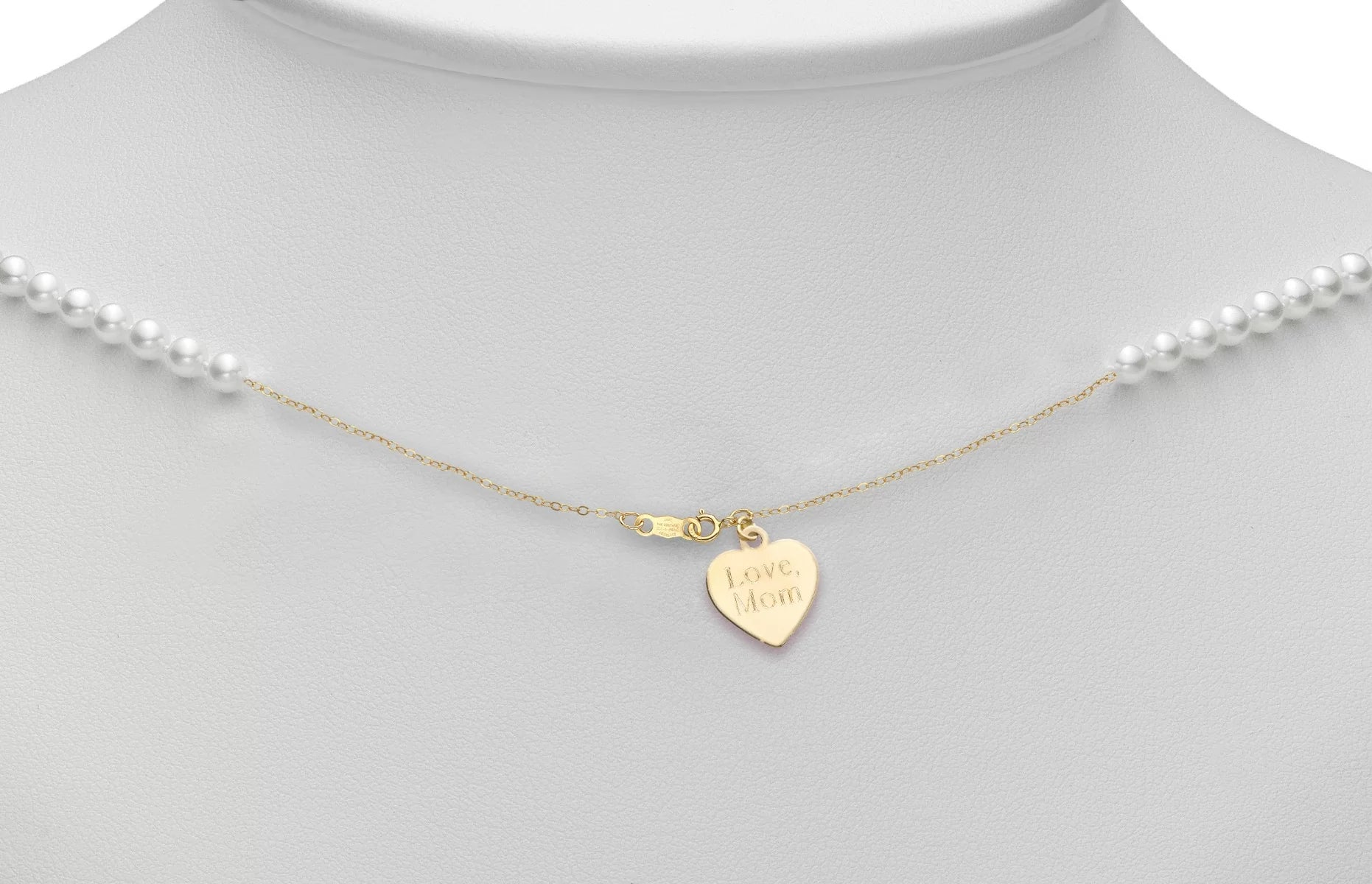 Gold heart-shaped pendant with 'Love, Mom' engraving on a pearl necklace.