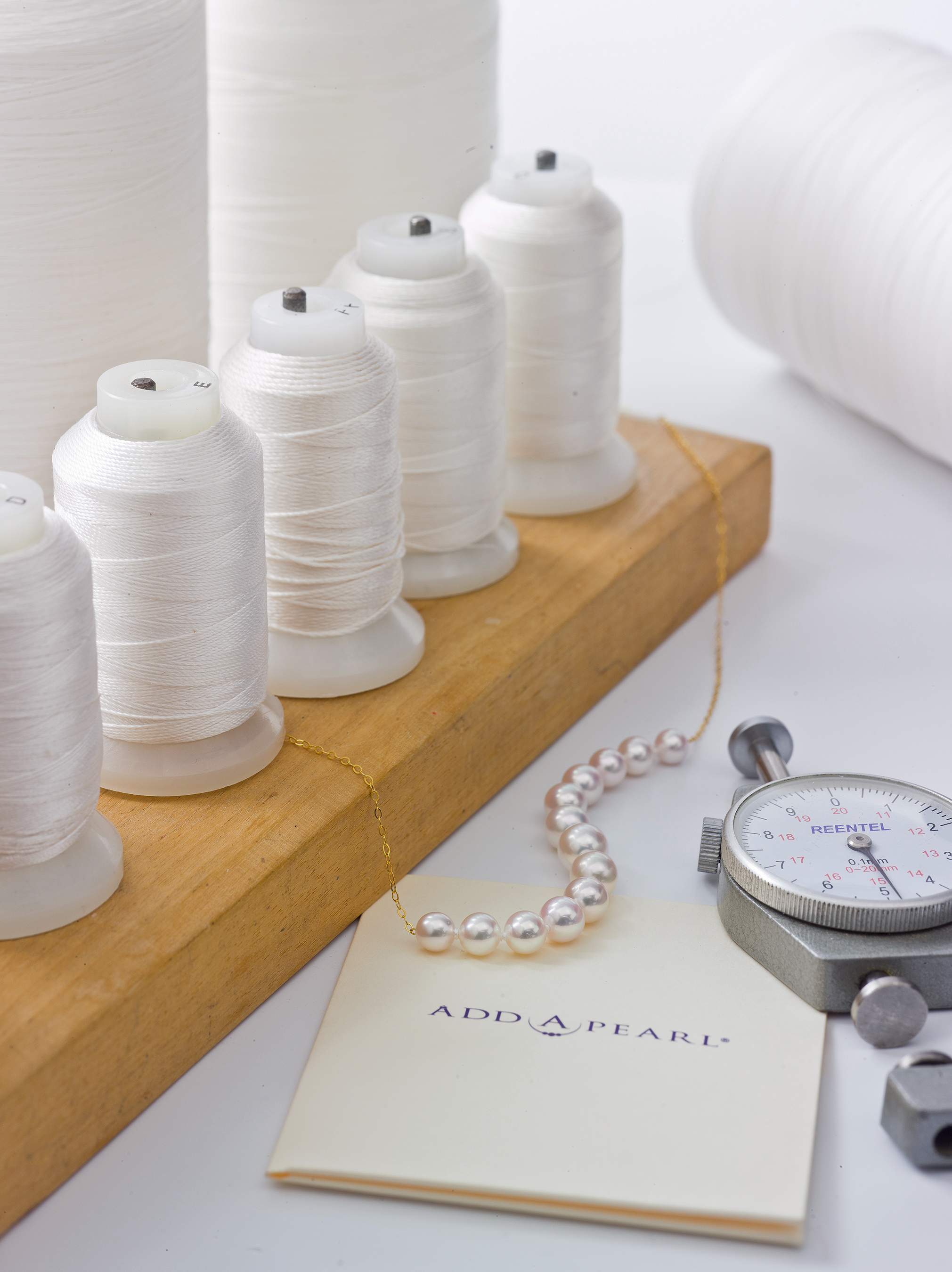 Silk thread spools, a precision caliper, and a finished pearl necklace on an Add-A-Pearl card in the Chicago atelier