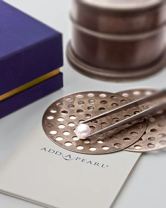 A pearl on an Add-A-Pearl card, with a box and jewelry tools in the background