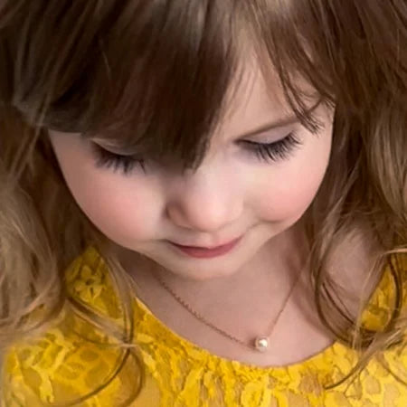 Close-up of a young girl wearing a yellow lace top with a gold single-pearl necklace.