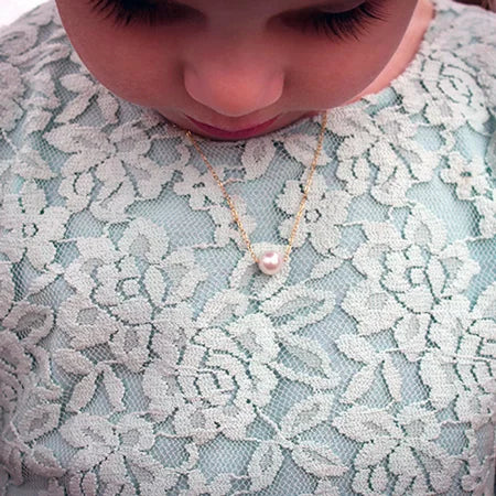 Close-up of a child wearing a single-pearl necklace on a lace garment.