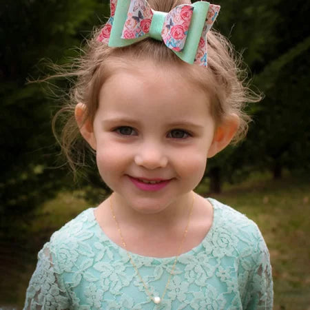 Young girl wearing a floral hair bow and a single-pearl necklace outdoors