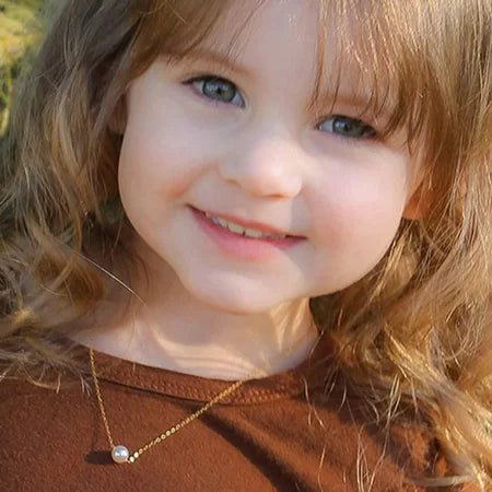Close-up of a child with a single-pearl necklace outdoors