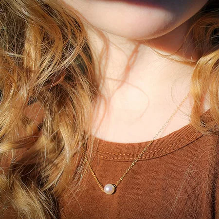 Close-up of a pearl necklace on a child with wavy hair and a brown top.