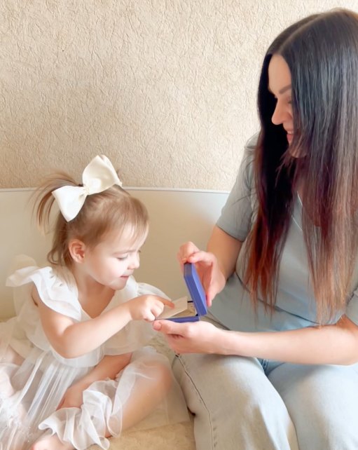 A little girl opening her Add-A-Pearl gift box with her mother