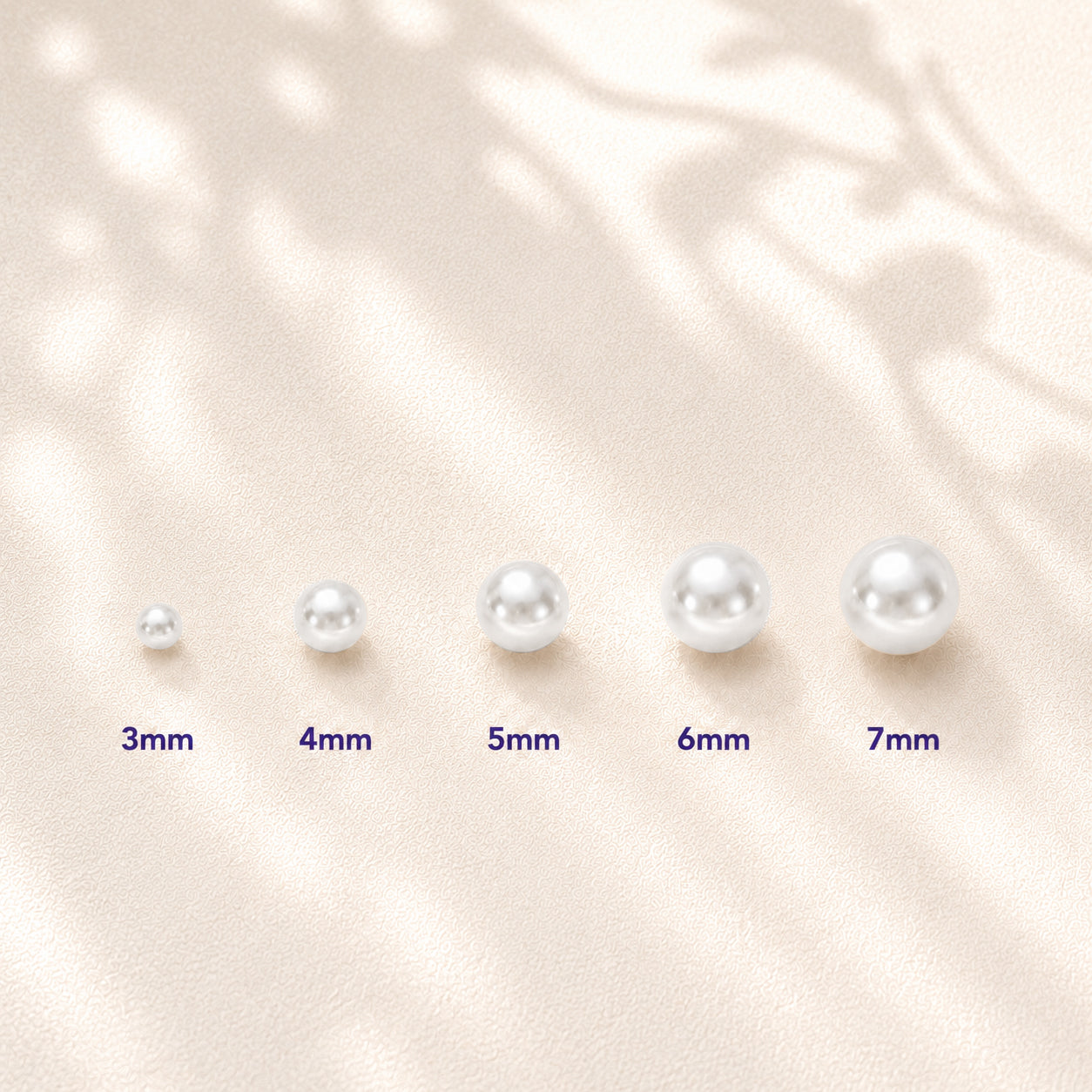 Five white pearl beads of increasing size labeled 3mm, 4mm, 5mm, 6mm, and 7mm, arranged on a soft beige textured background with leaf shadows.