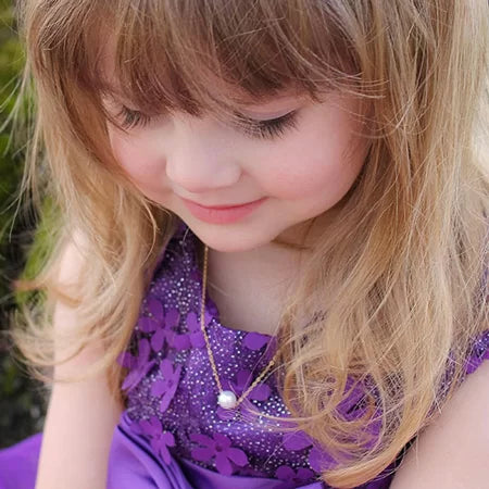 Young girl wearing a purple dress with floral patterns and a pearl necklace.