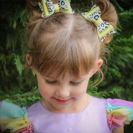 Child with colorful hair bows and a rainbow dress wearing a pearl necklace against a green background