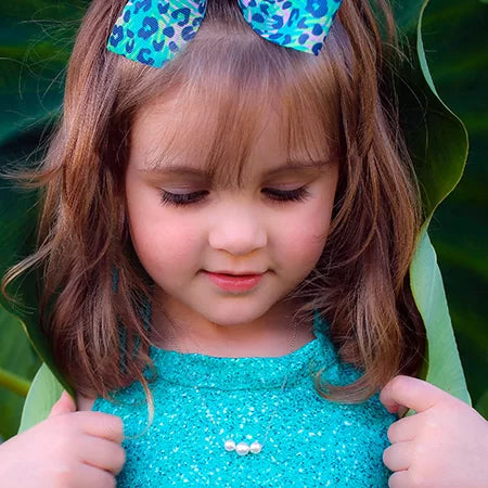 Young girl wearing a blue dress with a green bow in her hair, wearing a necklace with 3 graduated pearls.
