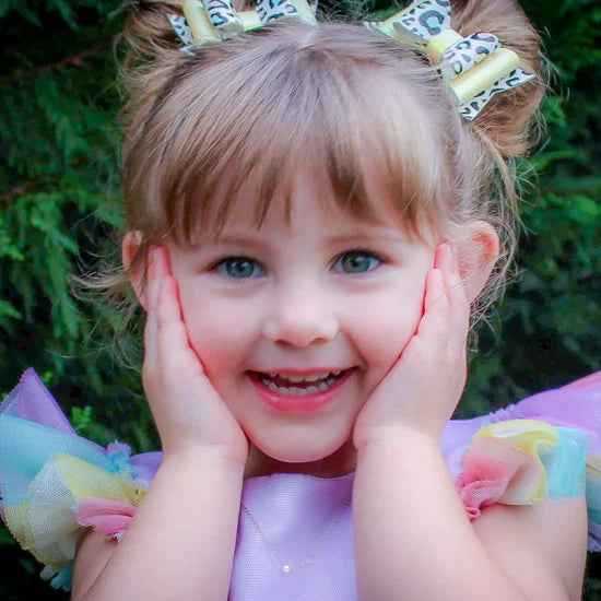 Young girl with colorful hair bows and a purple dress wearing a single-pearl necklace