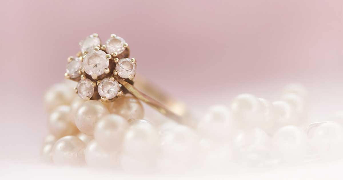 A ring with a cluster of diamonds sits atop a strand of pearls