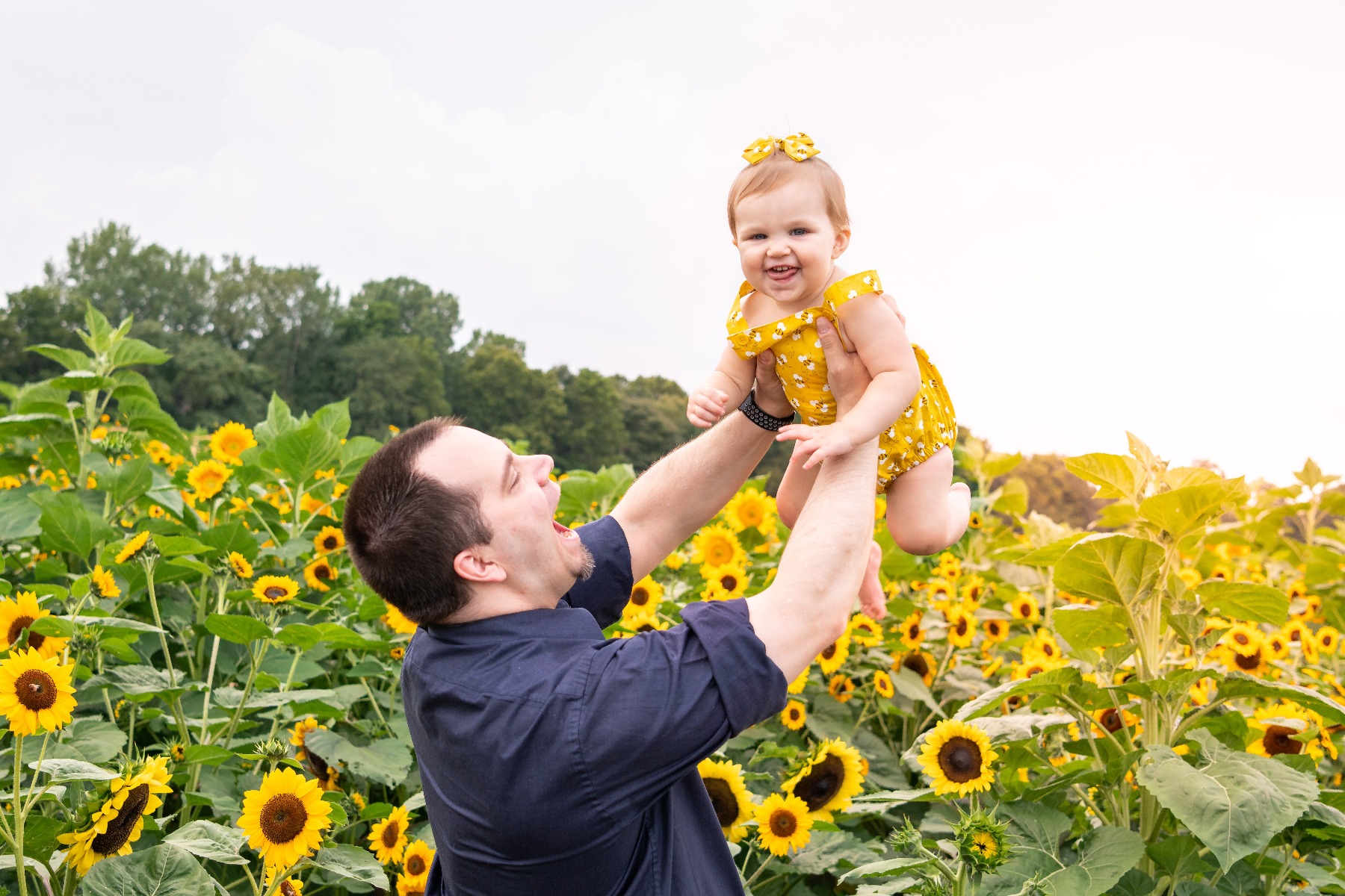 father and baby daughter are all smiles with a backdrop of sunflowers